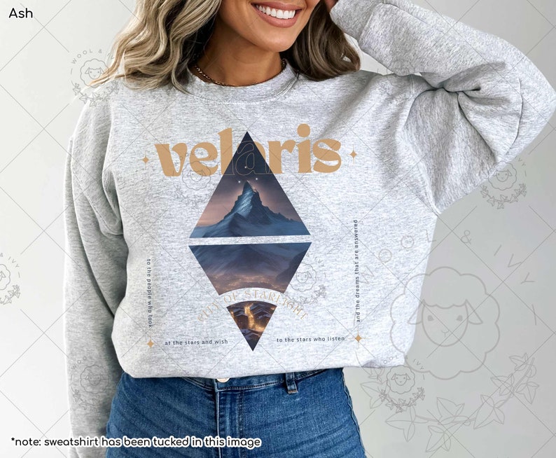 Puede incluir: Una sudadera gris con un dise&ntilde;o gr&aacute;fico de una cordillera monta&ntilde;osa y la palabra "velaris" en una fuente marr&oacute;n. El texto "to the people who took at the stars and wish to the stars who listen and the dreams that are answered" tambi&eacute;n est&aacute; impreso en la sudadera.