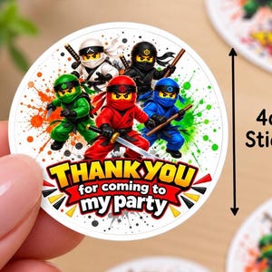 May include: A round 4cm sticker featuring five colourful ninja characters in green, white, black, red, and blue outfits. The design includes paint splatter accents and the text THANK YOU for coming to my party in bold yellow and white letters.