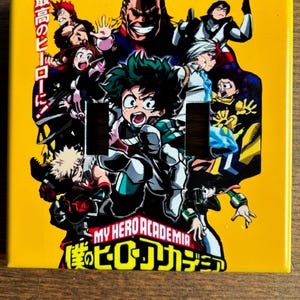May include: A yellow light switch cover with a graphic of characters from the anime My Hero Academia. The characters are in various poses and include All Might, Deku, and Bakugo. The text "My Hero Academia" and "僕のヒーローアカデミア" are printed on the cover.