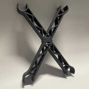 May include: A black, 3D printed, X-shaped structure with a geometric design. The structure has two arms that are bent at a 90-degree angle, creating a hook-like shape at each end.