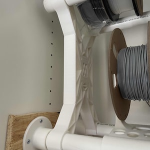 May include: White plastic shelf brackets with a white pipe attached to the bracket. The bracket is mounted to a wooden board with screws. The pipe is labelled "25F 1/2" and "ASTM D1985-21".