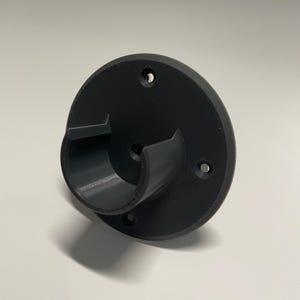 May include: A black plastic wall mount with a round base and a curved arm. The mount has four screw holes on the base.