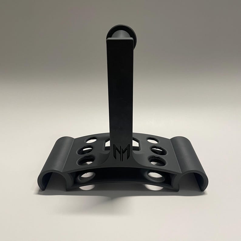 May include: Black plastic stand with a vertical post and a curved base with multiple holes. The stand has the letters "NM" printed on the front.