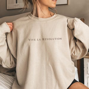May include: A beige sweatshirt with the text "VIVE LA RÉVOLUTION" printed in brown on the front.