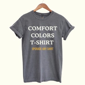 Puede incluir: Una camiseta gris oscuro con el texto "COMFORT COLORS T-SHIRT" en blanco y "UPGRADE ANY SHIRT" en amarillo.
