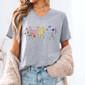 May include: A gray V-neck t-shirt with a rainbow floral print. The flowers are arranged in a row across the chest of the shirt.