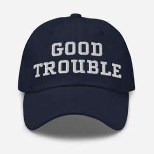 May include: A navy blue baseball cap with white embroidered text that reads "GOOD TROUBLE".