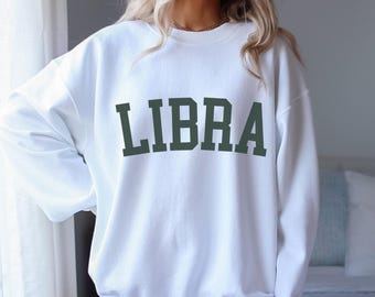 Op de afbeelding: Wit sweatshirt met het woord "LIBRA" in donkergroen op de voorkant.