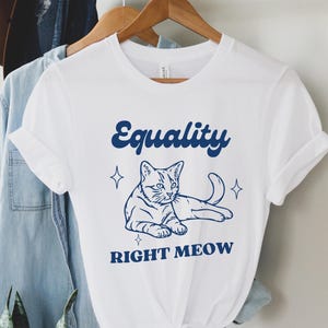 Pode incluir: Camiseta branca com um contorno azul de um gato e o texto "Equality Right Meow".