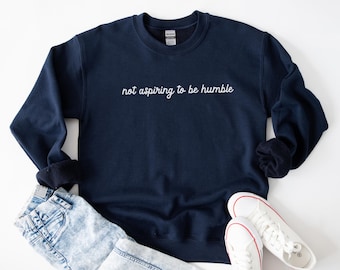 May include: A navy blue sweatshirt with the text "not aspiring to be humble" in white embroidery.