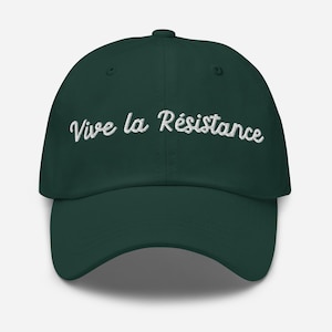 Pode incluir: Boné de beisebol verde escuro com aba curva. A frase "Vive la Résistance" é bordada em branco na frente. O boné tem um ajuste estruturado e um fecho de tira de tecido.
