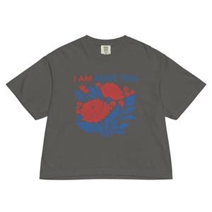 May include: Dark gray t-shirt with the text "I AM AUNT TIPA" in red and blue. The shirt features a floral design with red flowers and blue leaves. The shirt is made of a soft, comfortable material.