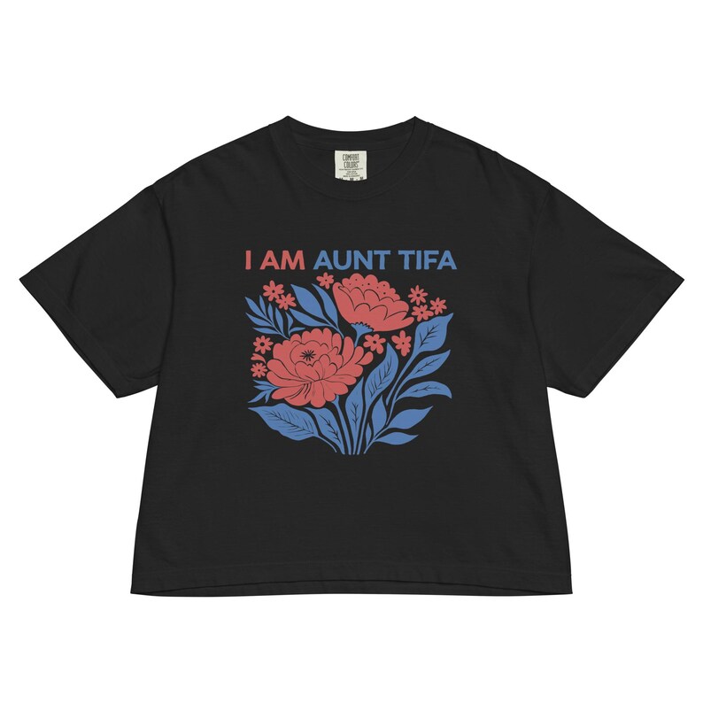 May include: Black t-shirt with the text "I AM AUNT TIFA" in red and blue. The shirt features a floral design with red flowers, blue leaves, and small red flowers. The shirt is a comfortable, casual style.