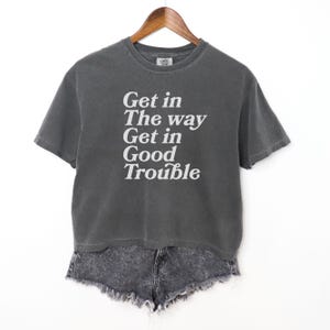以下が含まれることがあります： 白で「Get in The way Get in Good Trouble」とプリントされた、チャコールグレーのクロップドTシャツです。