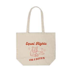 May include: A beige tote bag with a red graphic of a cat and the text "Equal Rights or I Bites".