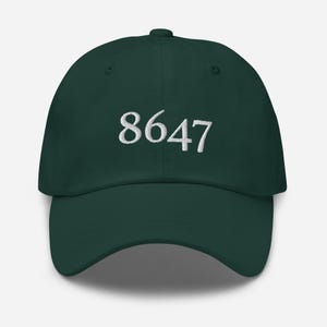 Puede incluir: Una gorra de béisbol verde oscuro con el número 8647 bordado en blanco en la parte delantera.