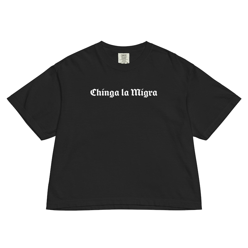 Pode incluir: T-shirt preto com a frase "Chinga la Migra" em letras g&oacute;ticas brancas. A camisa tem um corte folgado e mangas curtas. A pe&ccedil;a de roupa &eacute; feita de um material macio.