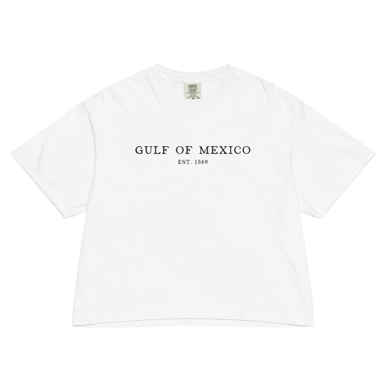 Op de afbeelding: Wit T-shirt met de tekst "GULF OF MEXICO" en "EST. 1569" in het zwart gedrukt. Het shirt heeft een ronde hals en korte mouwen. De stof lijkt zacht en comfortabel.