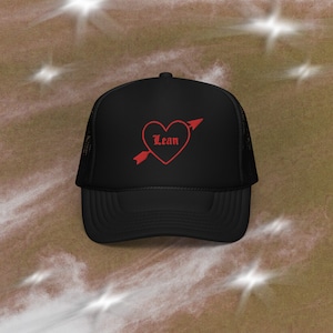 Puede incluir: Gorra de camionero negra con un diseño de corazón rojo y flecha. El corazón tiene la palabra "Lean" dentro.