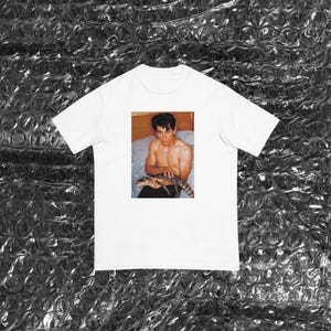 May include: White t-shirt featuring a photograph of a person holding an alligator.