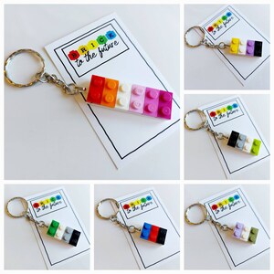 May include: A set of six colorful Lego brick keychains, each with a different color combination. The keychains are attached to silver key rings and have a white card with the text "Brick to the future" on them.