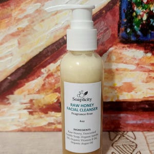 Puede incluir: Una botella de 4 onzas de limpiador facial de miel cruda con una tapa de bomba blanca. La botella está etiquetada "Soaplicity Raw Honey Facial Cleanser Fragrance Free 4oz Ingredients: Raw Honey, Unscented Castile Soap, Organic Jojoba Oil, Organic Vitamin E Oil, Organic Argan Oil"