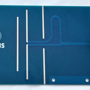 Könnte beinhalten: Eine blaue Leiterplatte mit einem weißen Pfeil, der nach links zeigt, und dem Text "arkis" mit einem drahtlosen Symbol. Die Platine hat ein Kupferspurmuster und zwei Löcher.