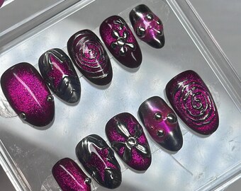 May include: A set of ten press-on nails featuring a deep magenta cat-eye magnetic finish. The nails are decorated with silver metallic 3D accents, including swirling lines, star shapes, floral patterns, and small spherical studs.