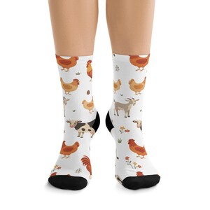 May include: White socks with a repeating pattern of farm animals, including chickens, cows, and goats. The socks have black heels and toes, and small floral accents are scattered throughout the design. The overall theme is a farm or countryside aesthetic.