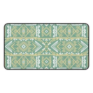 Op de afbeelding: Rechthoekige decoratieve mat met een geometrisch tribaal patroon. Het ontwerp bevat herhaalde vormen in tinten groen, crème en wit. De rand is zwart.