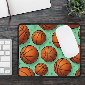 May include: Rectangular mousepad featuring a pattern of orange basketballs on a light green background with black trim. A white computer mouse rests on the pad. The design includes a variety of basketball sizes.