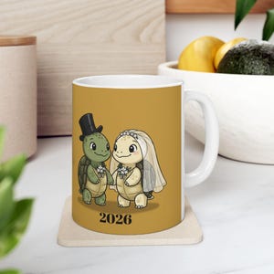May include: White ceramic mug featuring a cartoon turtle couple in wedding attire, holding hands. The groom turtle wears a black top hat, and the bride turtle has a veil. The year "2026" is printed below the couple.