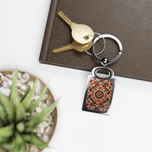 Op de afbeelding: Een zilveren sleutelhanger met een rechthoekig label met een kleurrijk mandala-ontwerp. Het label heeft een zilveren ring en een zilveren lus om sleutels aan te bevestigen.