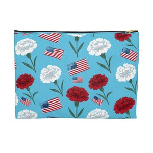 May include: A rectangular zippered pouch with a light blue background. The pouch is patterned with red and white carnation flowers and American flags. The zipper is gold-colored.
