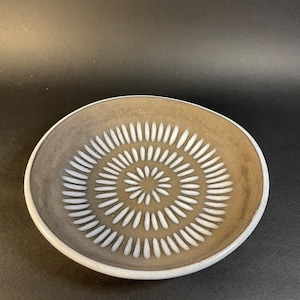 Könnte beinhalten: Eine weiße Keramikschale mit brauner Glasur und einem weißen, geprägten Design eines Kreises mit strahlenden Linien.