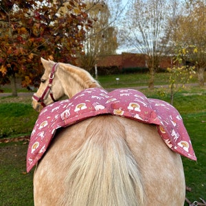 May include: A pink horse saddle pad with a unicorn and rainbow pattern. The pad is on a horse's back.