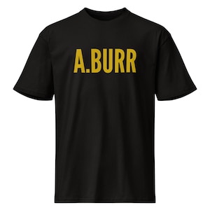 Puede incluir: Una camiseta negra de manga corta con el texto A.BURR impreso en una fuente sans-serif de color amarillo mostaza en el pecho. La prenda cuenta con un cuello redondo clásico y un dobladillo recto, mostrando un diseño sencillo.
