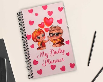 May include: A pink spiral bound notebook with a cartoon couple holding red heart balloons. The notebook says "My Daily Planner" in pink lettering.