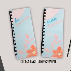 May include: Two spiral bound notebooks with a blue background and pink and orange floral designs. The notebook on the left says "to remember" and the notebook on the right says "para recordar".