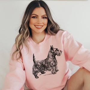 May include: A pink sweatshirt with a black and white illustration of a Scottish Terrier dog.