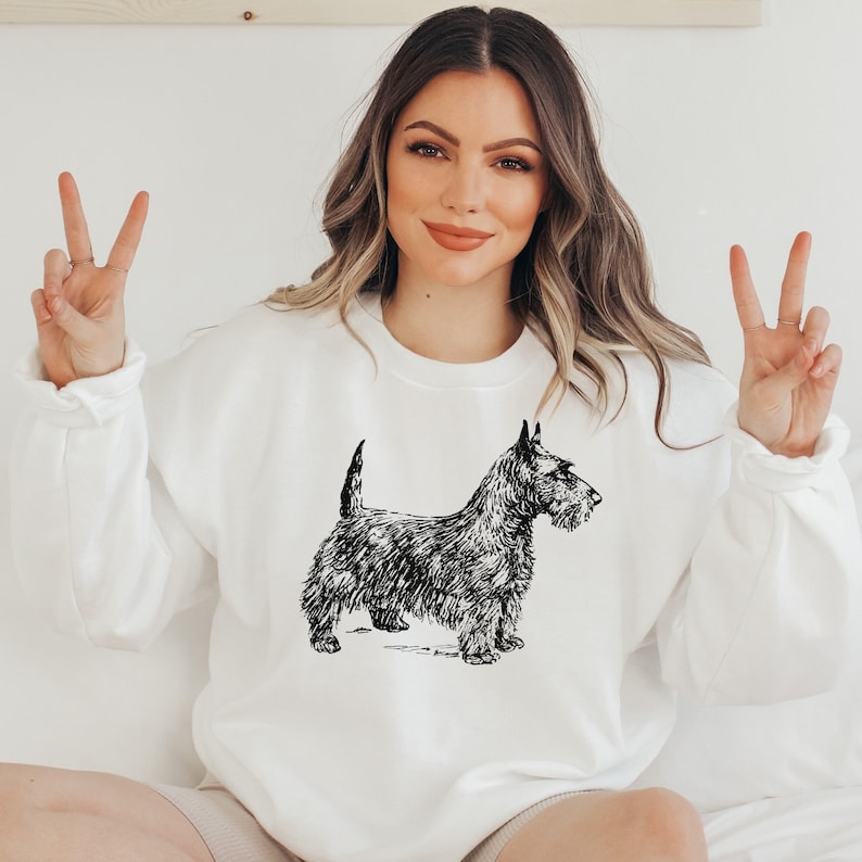 May include: A white sweatshirt with a black and white illustration of a Scottish Terrier dog.