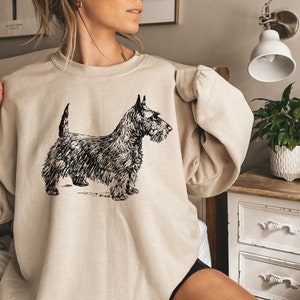 May include: A beige sweatshirt with a black and white illustration of a Scottish Terrier dog.