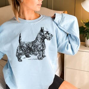 May include: A light blue sweatshirt with a black and white illustration of a Scottish Terrier.