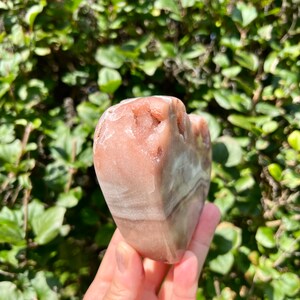 May include: A heart-shaped pink and white banded agate crystal. The crystal has a rough, natural texture.