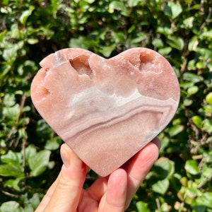 May include: A heart-shaped pink and white crystal with natural druzy inclusions. The crystal is polished and has a smooth surface.