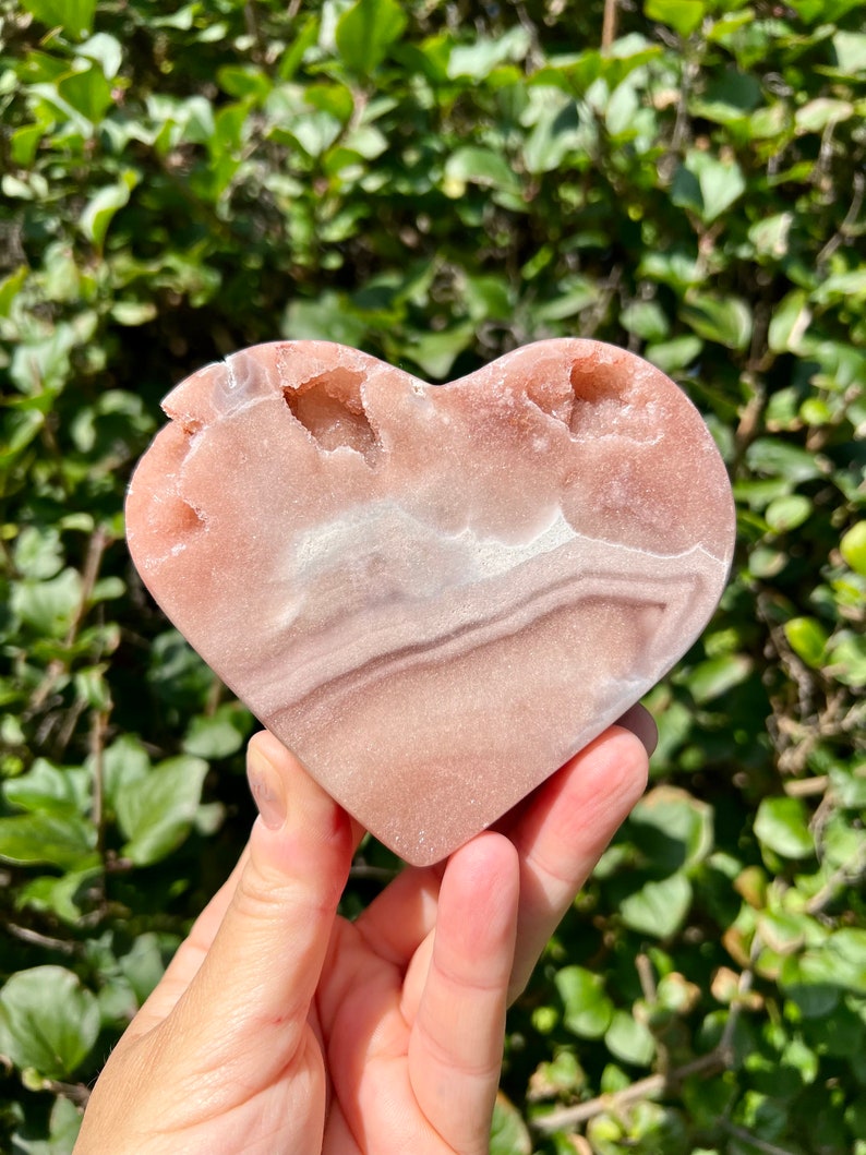May include: A heart-shaped pink and white crystal with natural druzy inclusions. The crystal is polished and has a smooth surface.