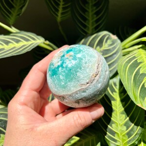 May include: A green and white agate sphere with a swirling pattern. The sphere is smooth and polished.