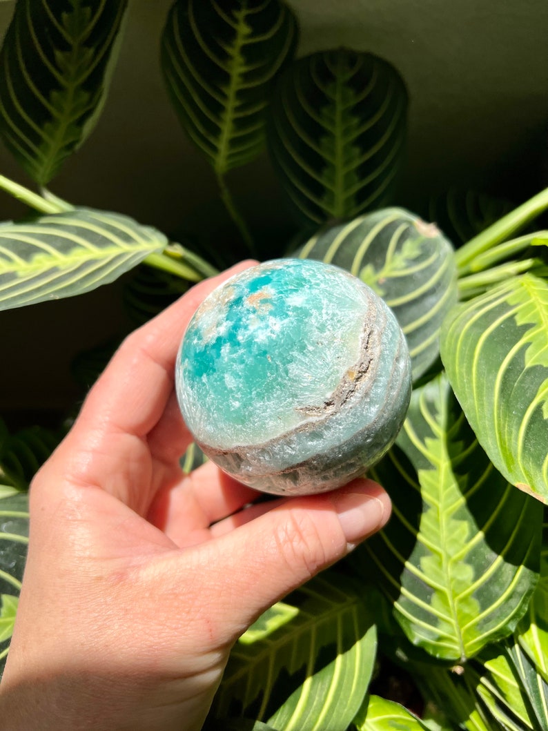 May include: A green and white agate sphere with a swirling pattern. The sphere is smooth and polished.