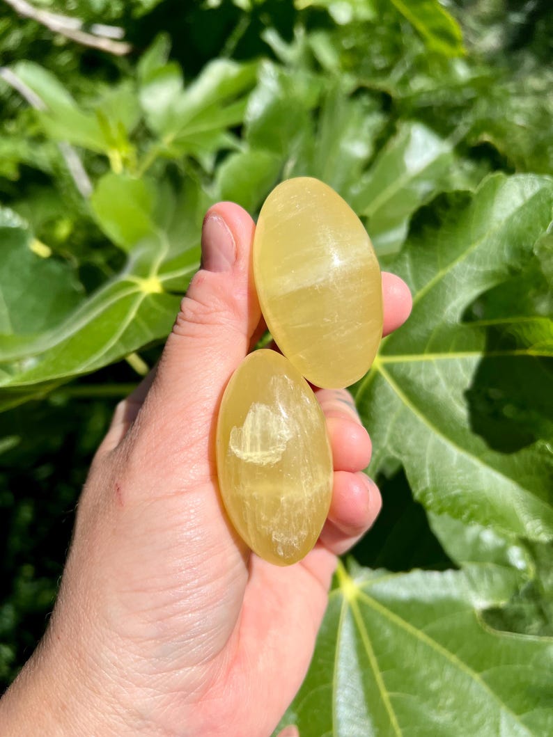 May include: Two yellow oval-shaped polished stones with white streaks. The stones are smooth and have a glossy finish.