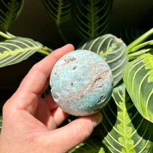 May include: A green and white agate sphere with a swirling pattern. The sphere is smooth and polished.
